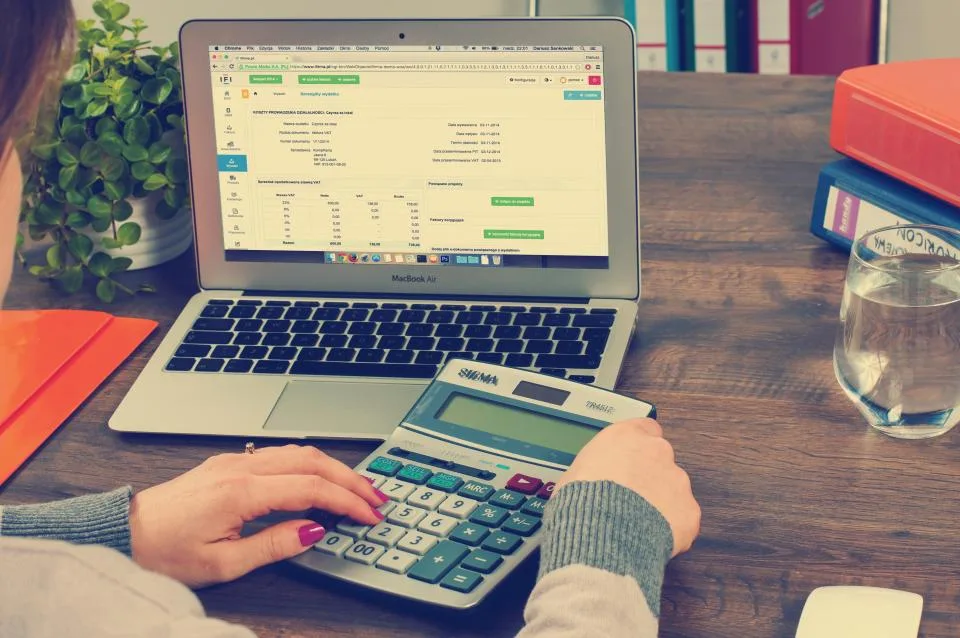 Person using a desk calculator in front of a laptop showing a spreadsheet