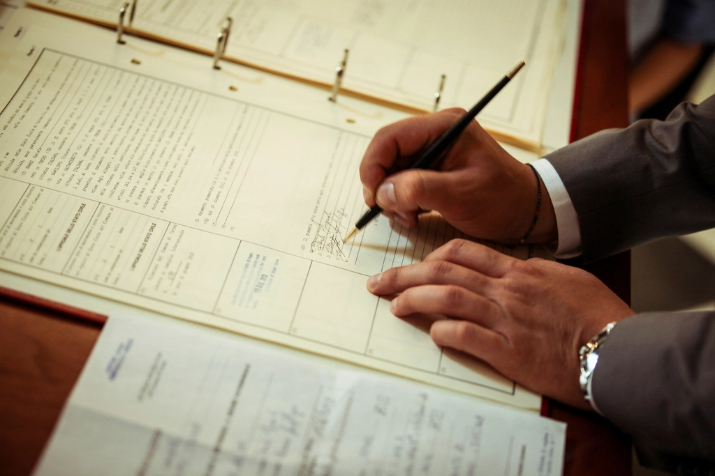 Hands signing a printed agreement in a ring binder on a desk