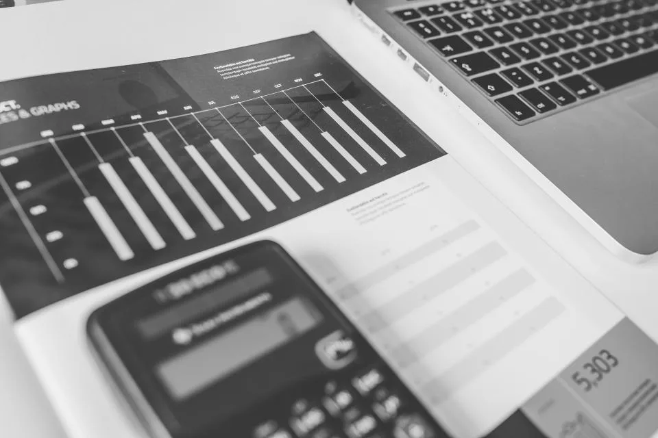 Calculator resting on printed financial charts next to a laptop