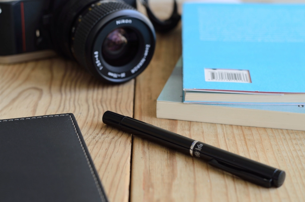 Camera, notebook and pen on a light wooden desk