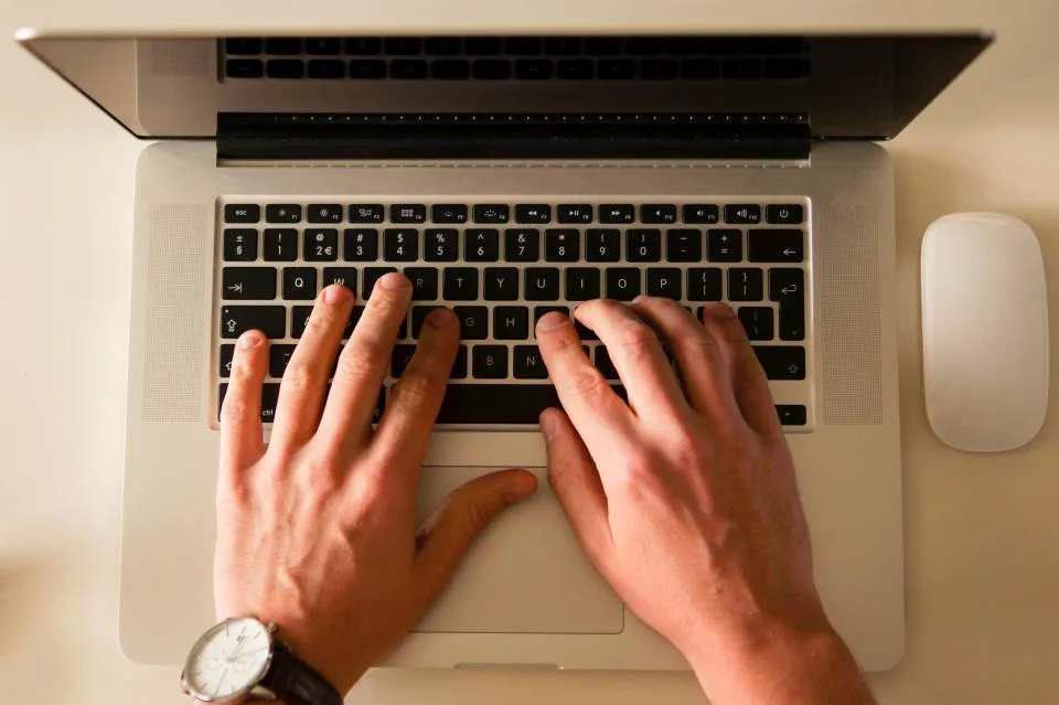 Hands typing on a laptop keyboard next to a mouse, seen from above