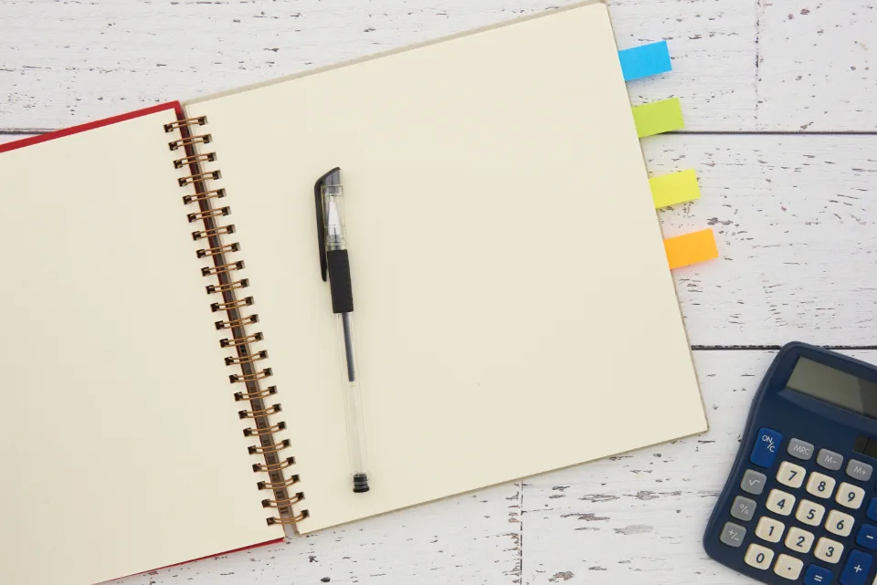Open spiral notebook with a pen, colored tabs and a calculator on a white desk