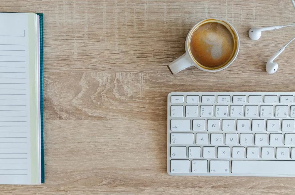 Open lined notebook beside a keyboard and a cup of coffee on a light wooden desk