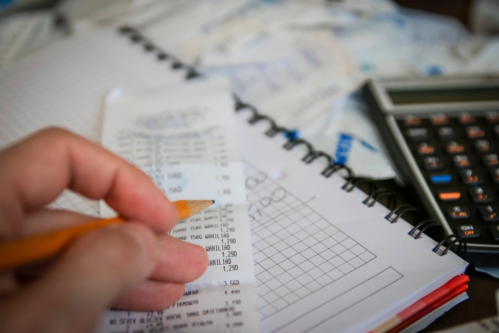 Hand holding a pencil and a receipt over a grid notebook next to a calculator
