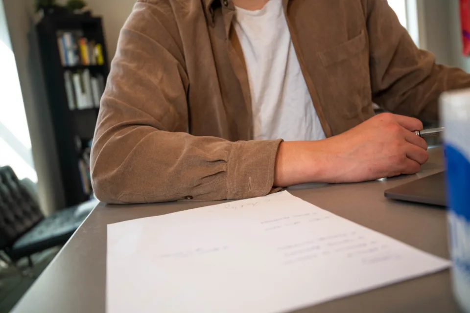 Person at an office desk reviewing a printed document with a pen
