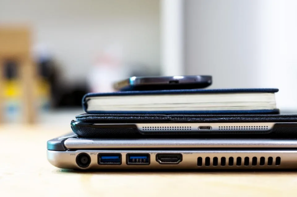 Stack of a laptop, tablet, notebook and phone on a bright desk